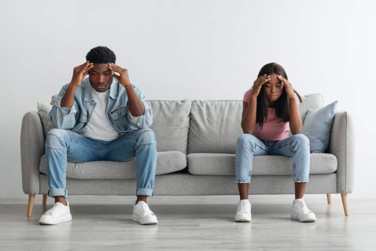 Depressed young black couple sitting on couch and thinking